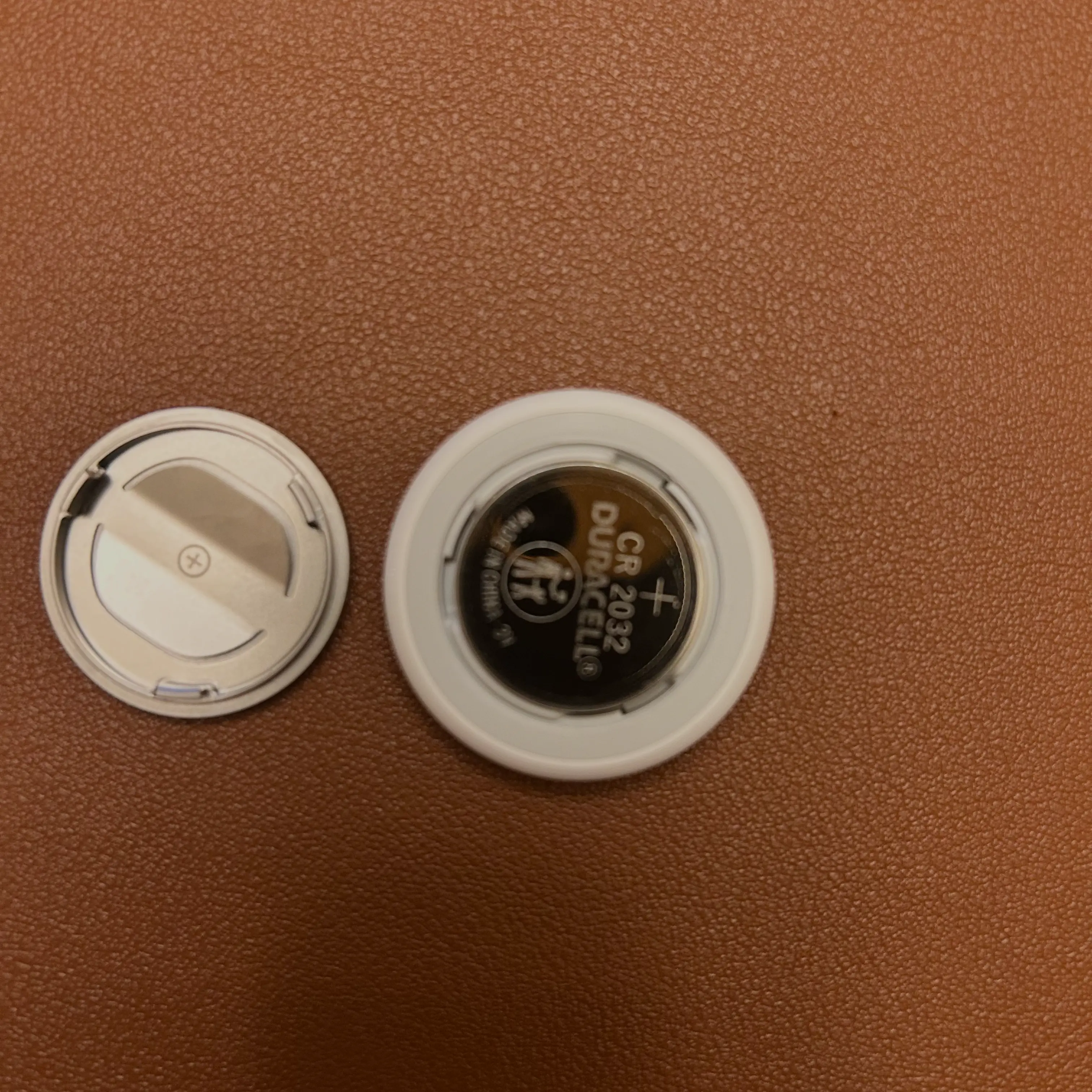 TThe AirTag with a new CR2032 battery inserted into the battery compartment, next to the metal cover that has been removed.