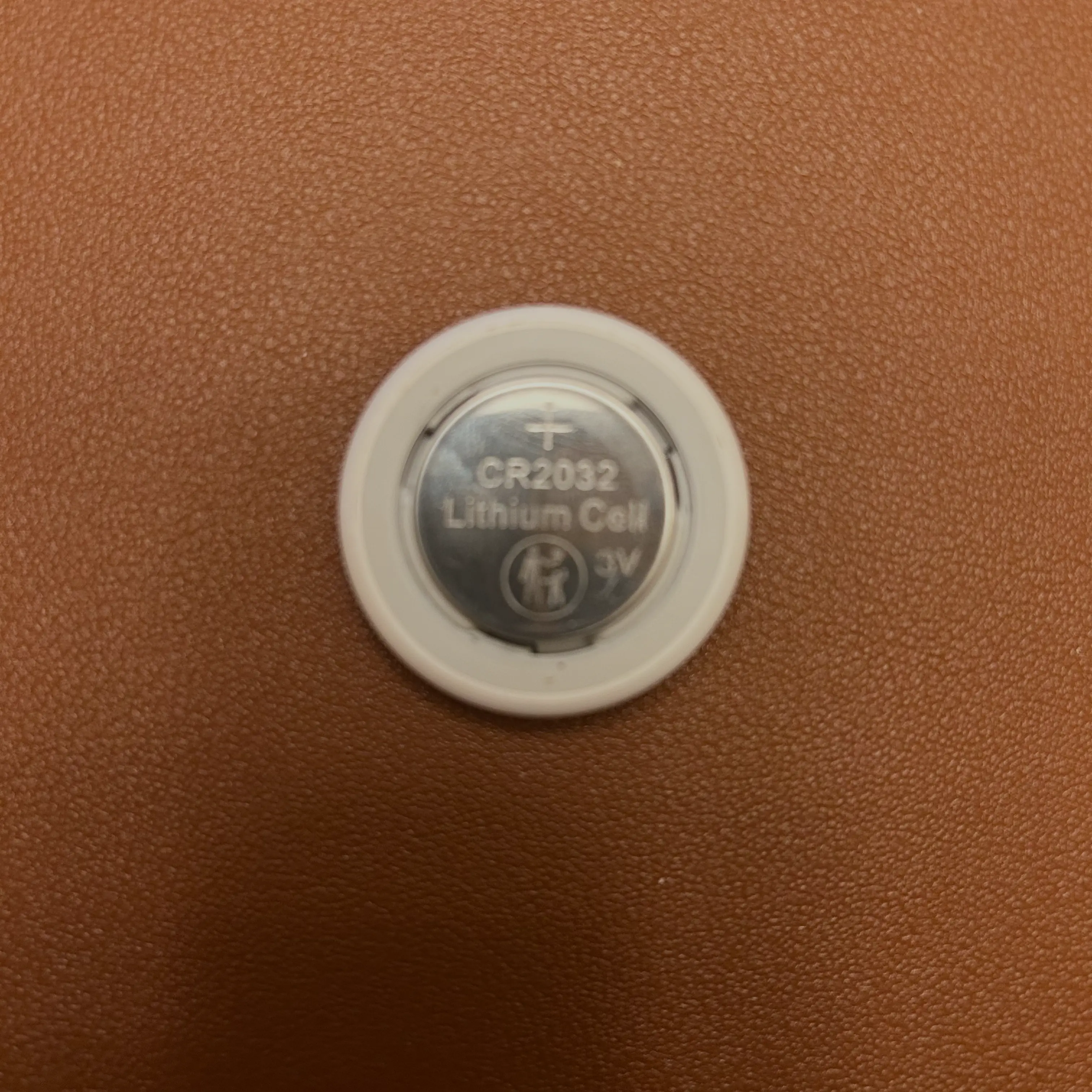 The back of an AirTag after the metal cover has been removed, revealing a CR2032 lithium battery still inside the AirTag's compartment.