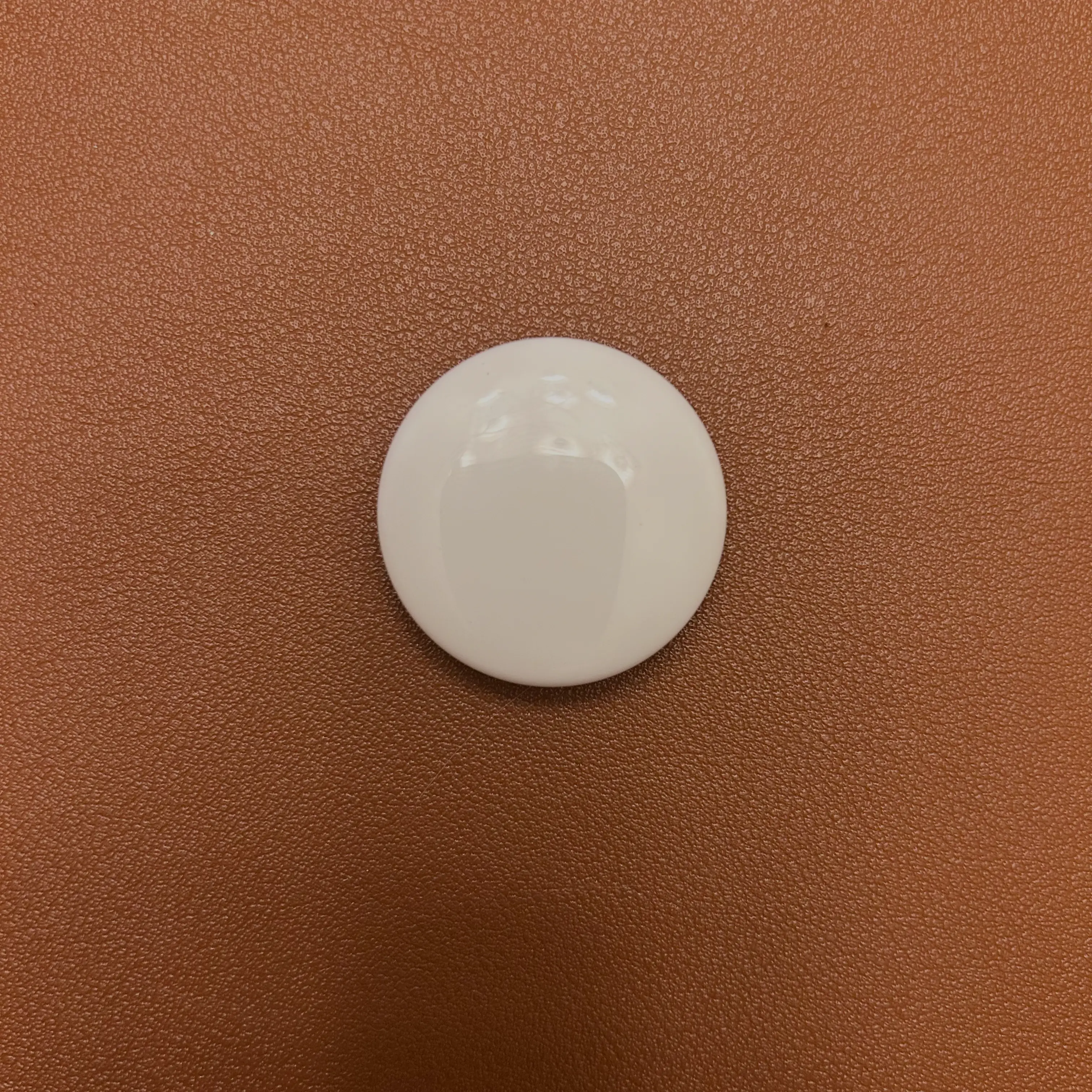 A close-up view of an intact AirTag, with the white plastic front facing up, placed on a brown surface.